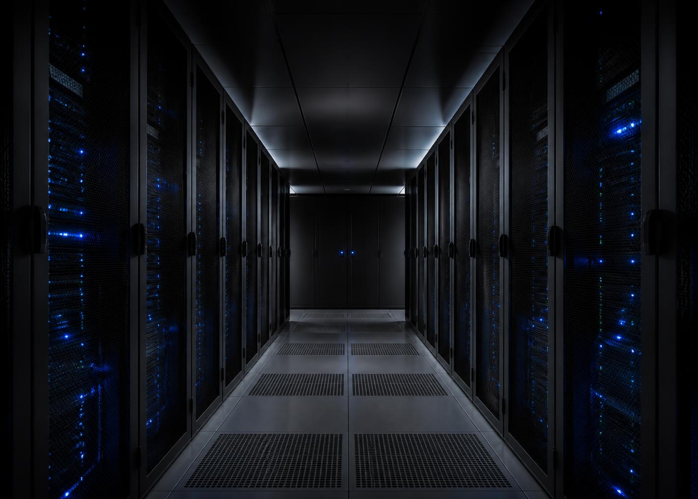 Corridor of server racks in a data centre lit by small blue status indicators